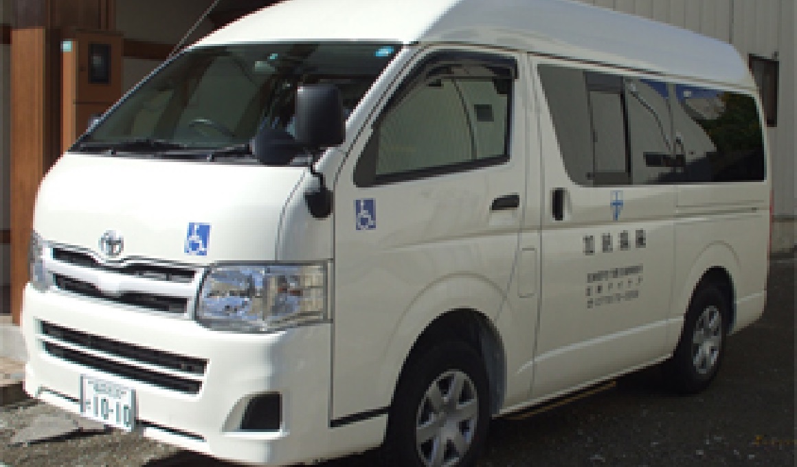 介護施設の送迎用白色マイクロバス。外構駐車スペースに停車している。